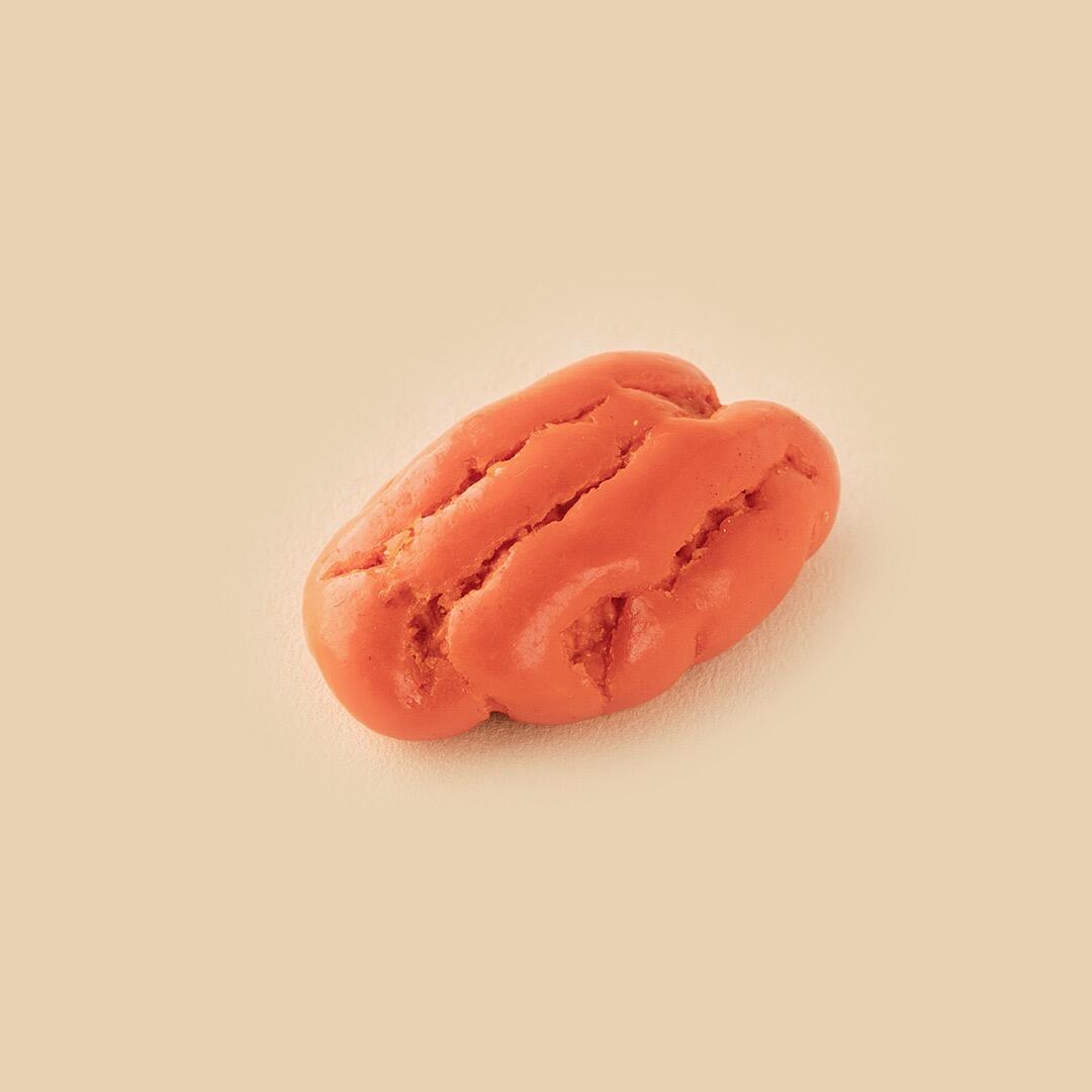 A single orange, textured pecan nut coated in a smooth, vibrant citrus glaze centered against a minimalist beige studio background