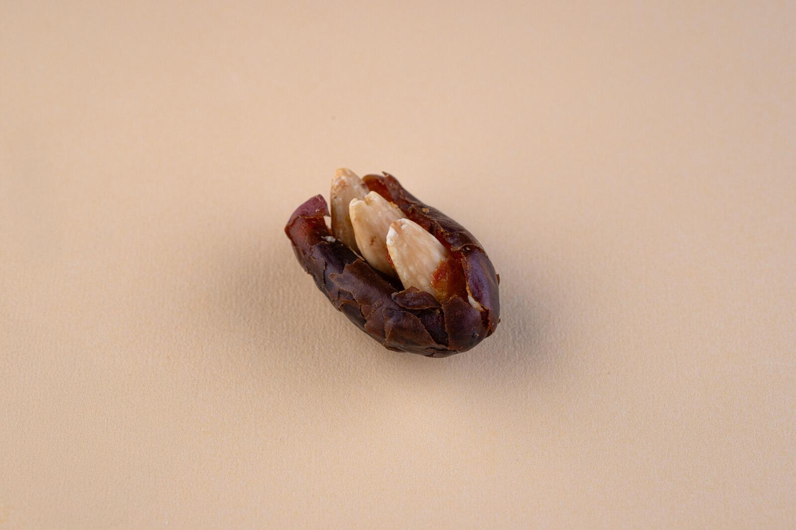 A single Khudri date stuffed with blanched almonds centered on a plain, light beige background in a high-angle studio shot