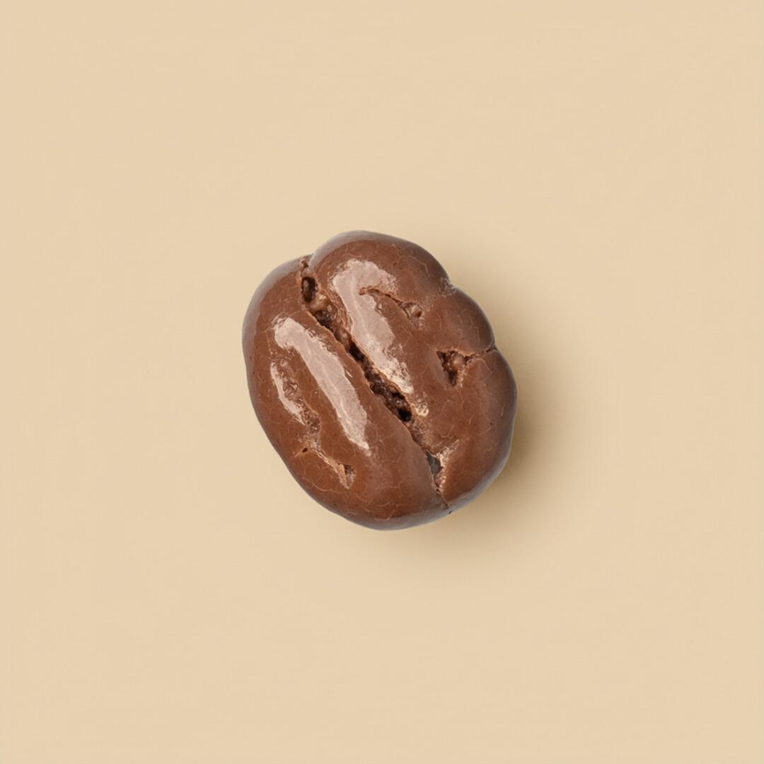 A single, shiny milk chocolate-coated coffee bean dragee centered on a solid beige background, viewed from directly above.