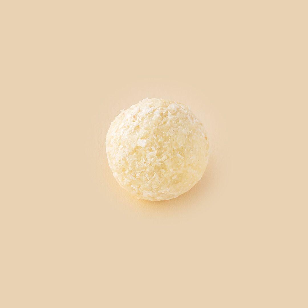 A single round confection coated in shredded coconut, centered against a solid light beige background, viewed from directly above