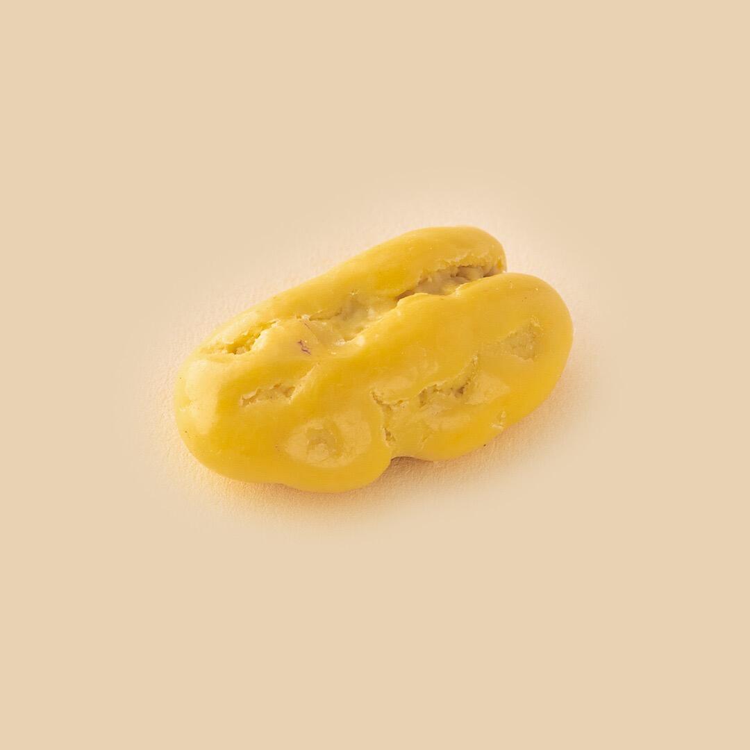 A single light yellow glazed pecan nut dragée on a plain beige background, viewed from a slightly elevated angle