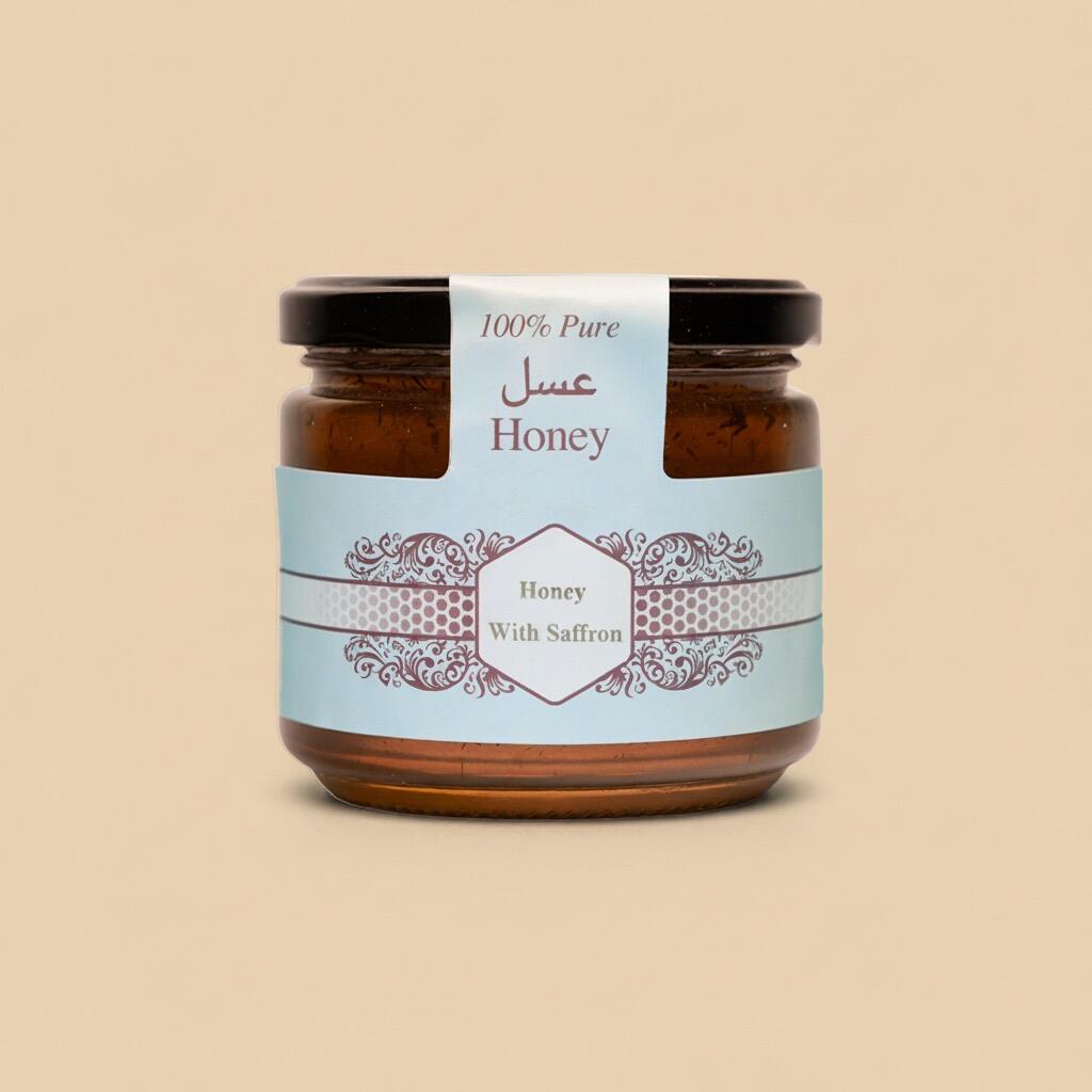 Small glass jar of honey with saffron, featuring a blue label with Arabic and English text, centered on a solid beige background.