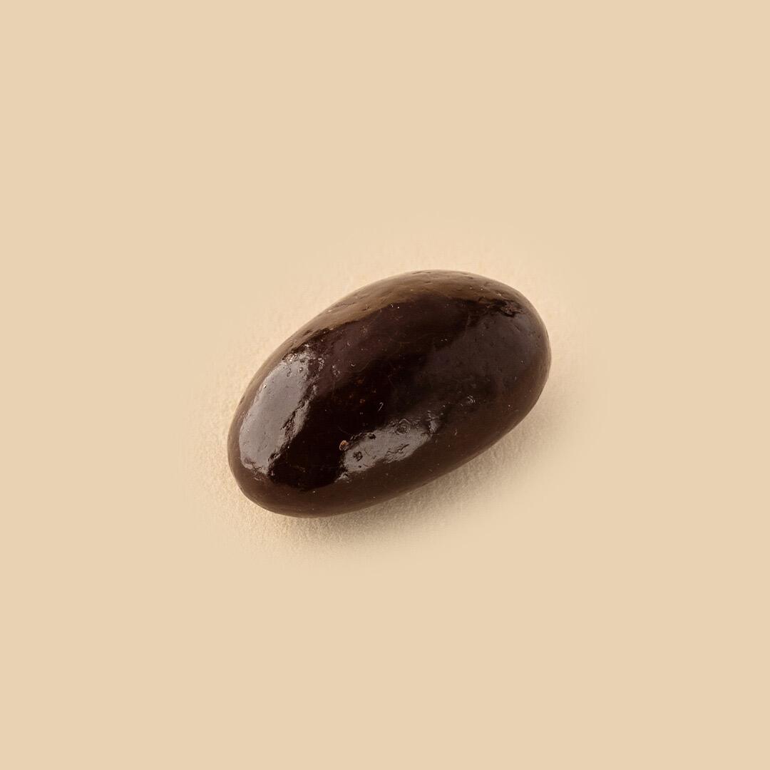 A single dark chocolate-covered almond dragee shown from a high-angle view on a smooth, neutral cream-colored background