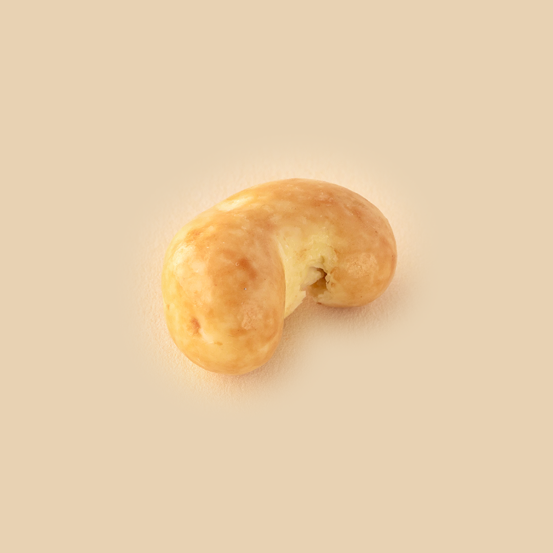 A single cashew nut coated in a smooth, glossy light-brown caramel glaze, centered on a neutral beige background