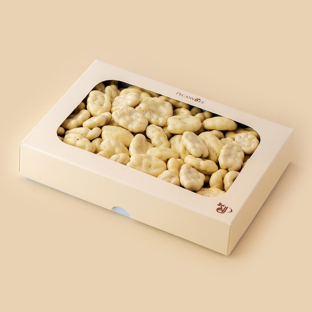 A white rectangular box with a transparent window filled with white chocolate-coated pecan dragees set against a solid beige background