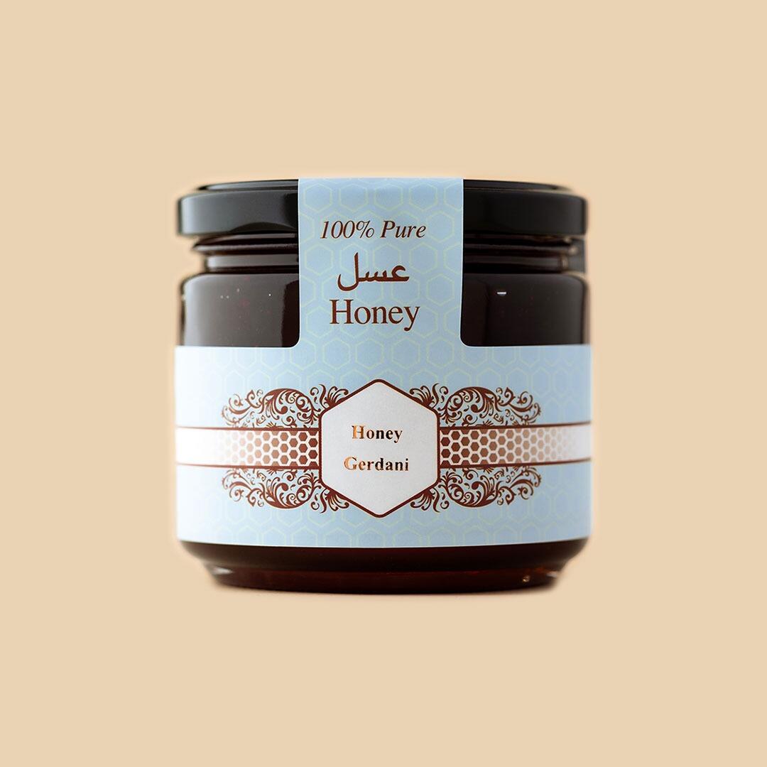A small glass jar of Gerdani honey with a black lid and a light blue hexagonal patterned label against a soft beige background