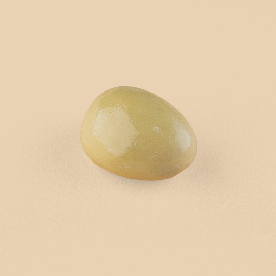A single, oval-shaped cappuccino-covered date with a smooth, glossy light-brown finish centered against a matching beige background