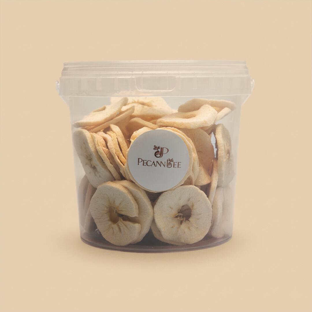 A clear, cylindrical plastic container filled with light-colored dried apple slices, featuring a round white PecanBee logo label, set against a solid beige back