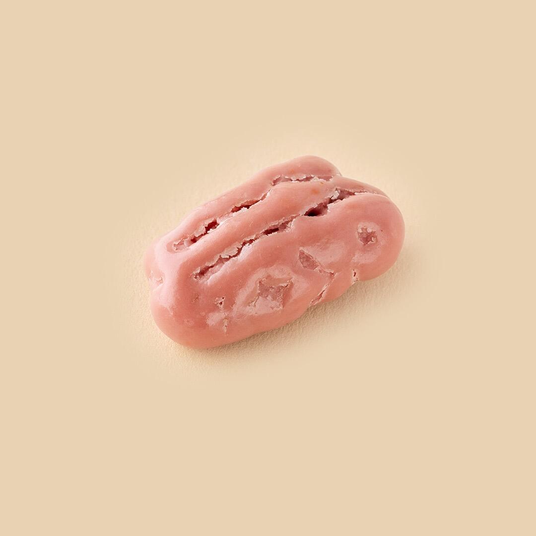 A single ruby chocolate-coated pecan nut centered on a solid, light beige background shown from a high-angle view