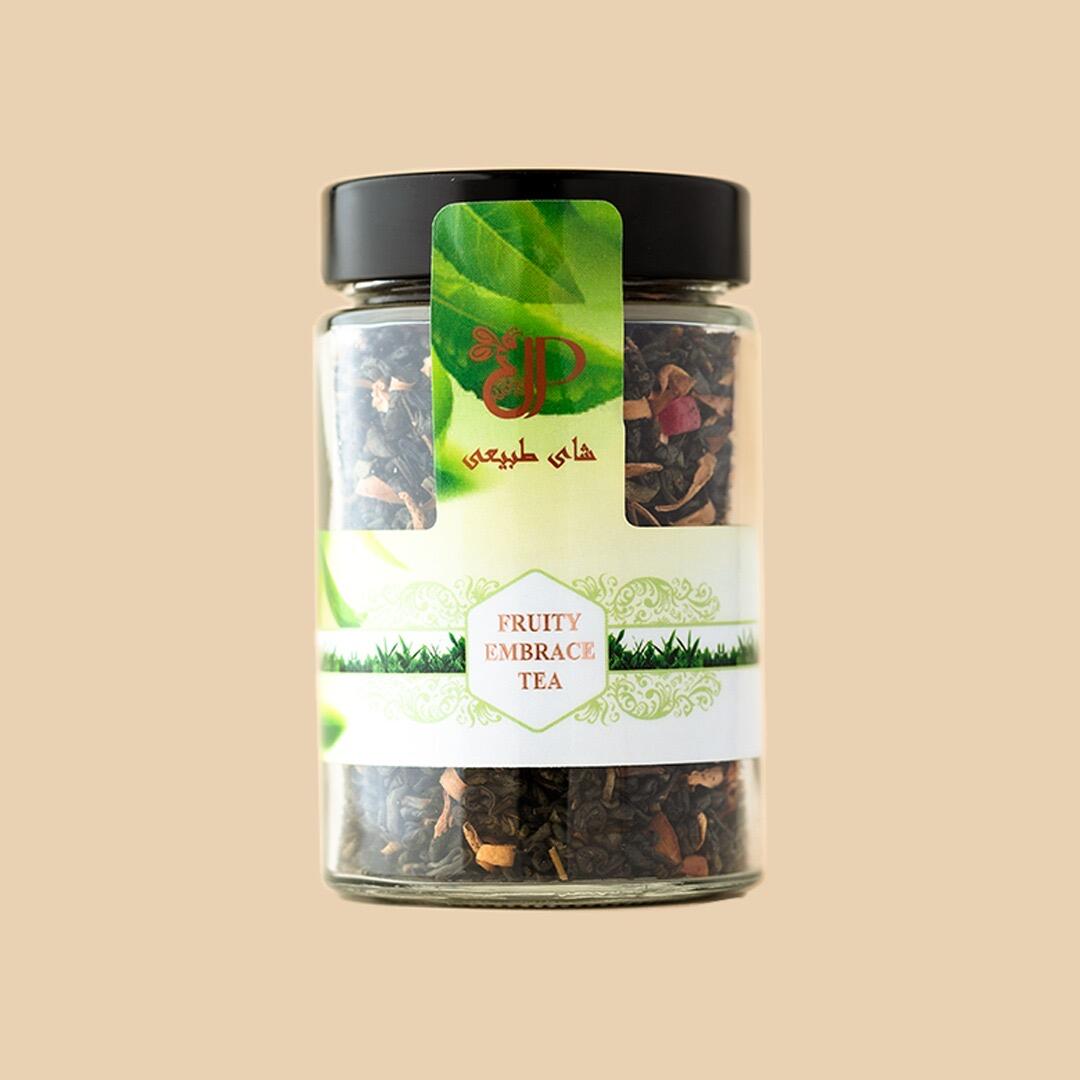 A clear glass jar filled with dark loose-leaf tea mixed with dried fruit pieces, featuring a green branded label with text in English and Persian against a beig