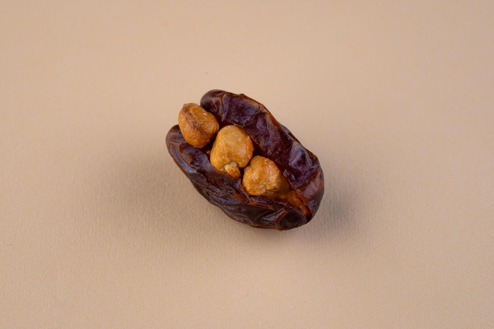 A single pitted Medjool date stuffed with three roasted chickpeas, centered on a minimalist beige background, viewed from a high angle.