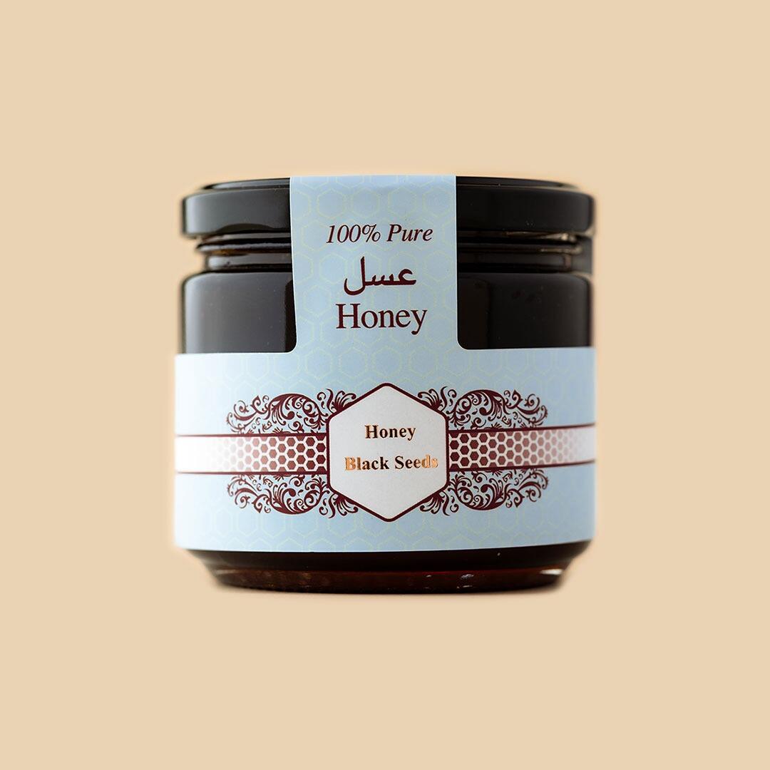 A glass jar of honey with a dark brown lid and a light blue label featuring honeycomb patterns, floral borders, and the text 100% Pure Honey and Black Seeds.