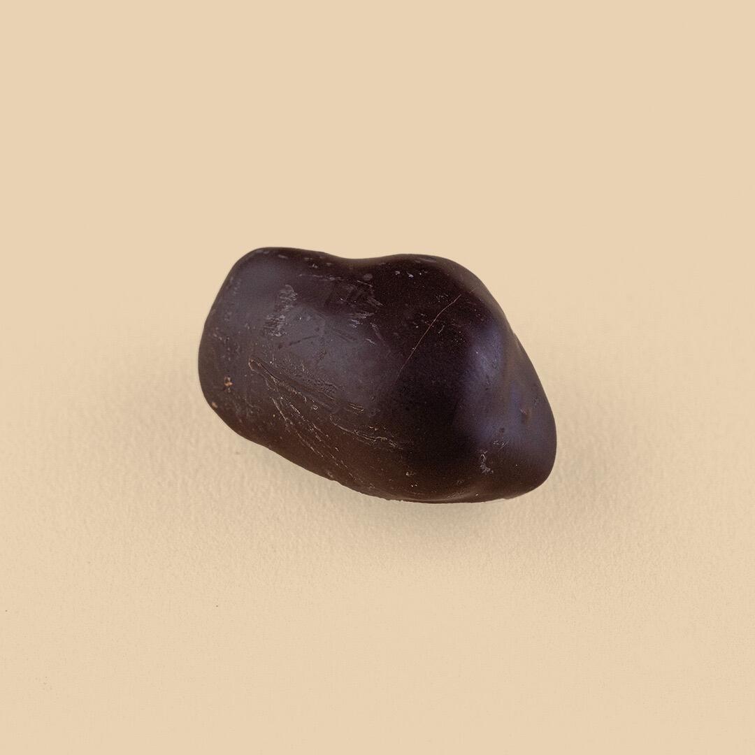 A single dark chocolate-covered date with a smooth, glossy finish, captured at a slight angle against a solid, light beige background