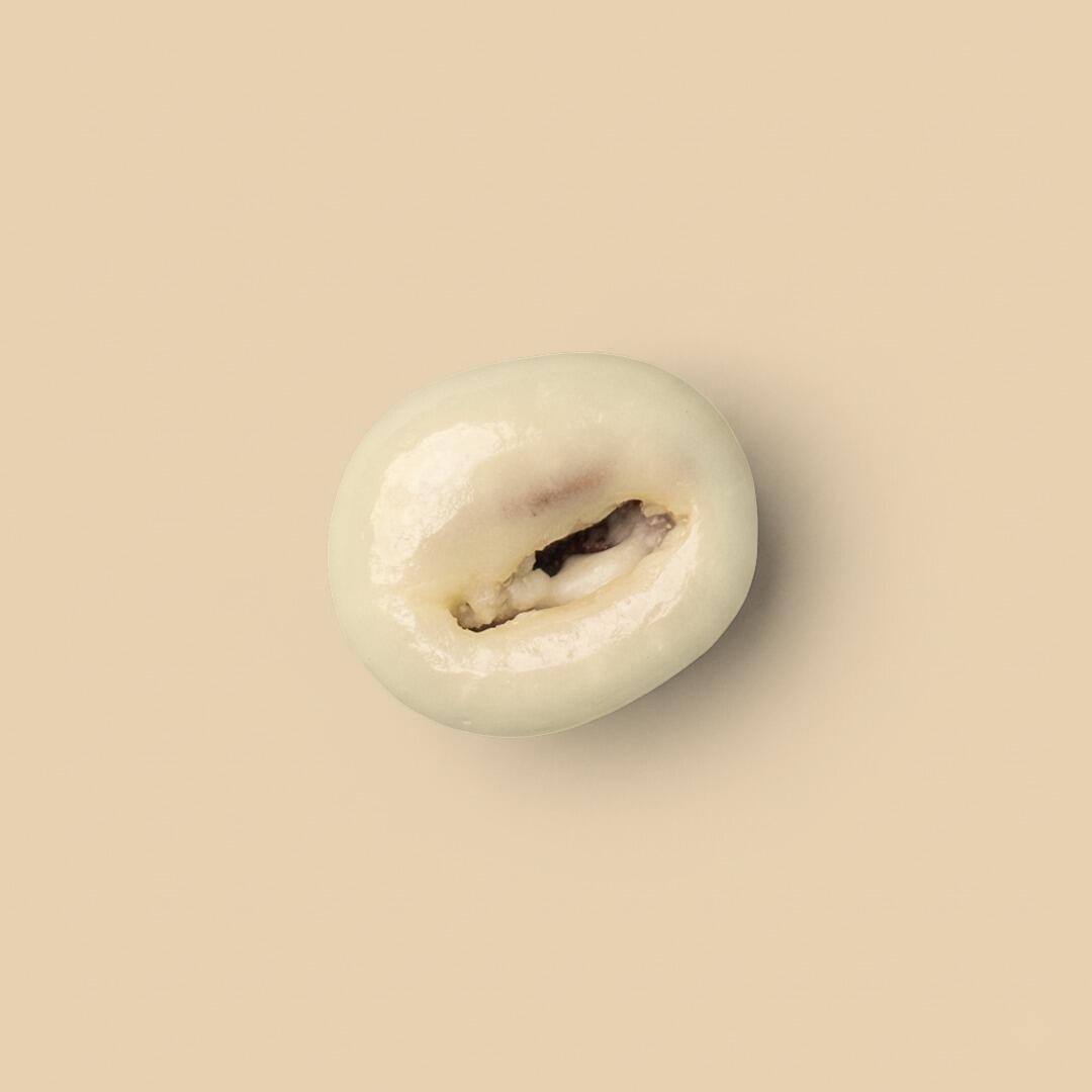 A single coffee bean coated in smooth white chocolate, shown from a top-down perspective against a solid light beige background