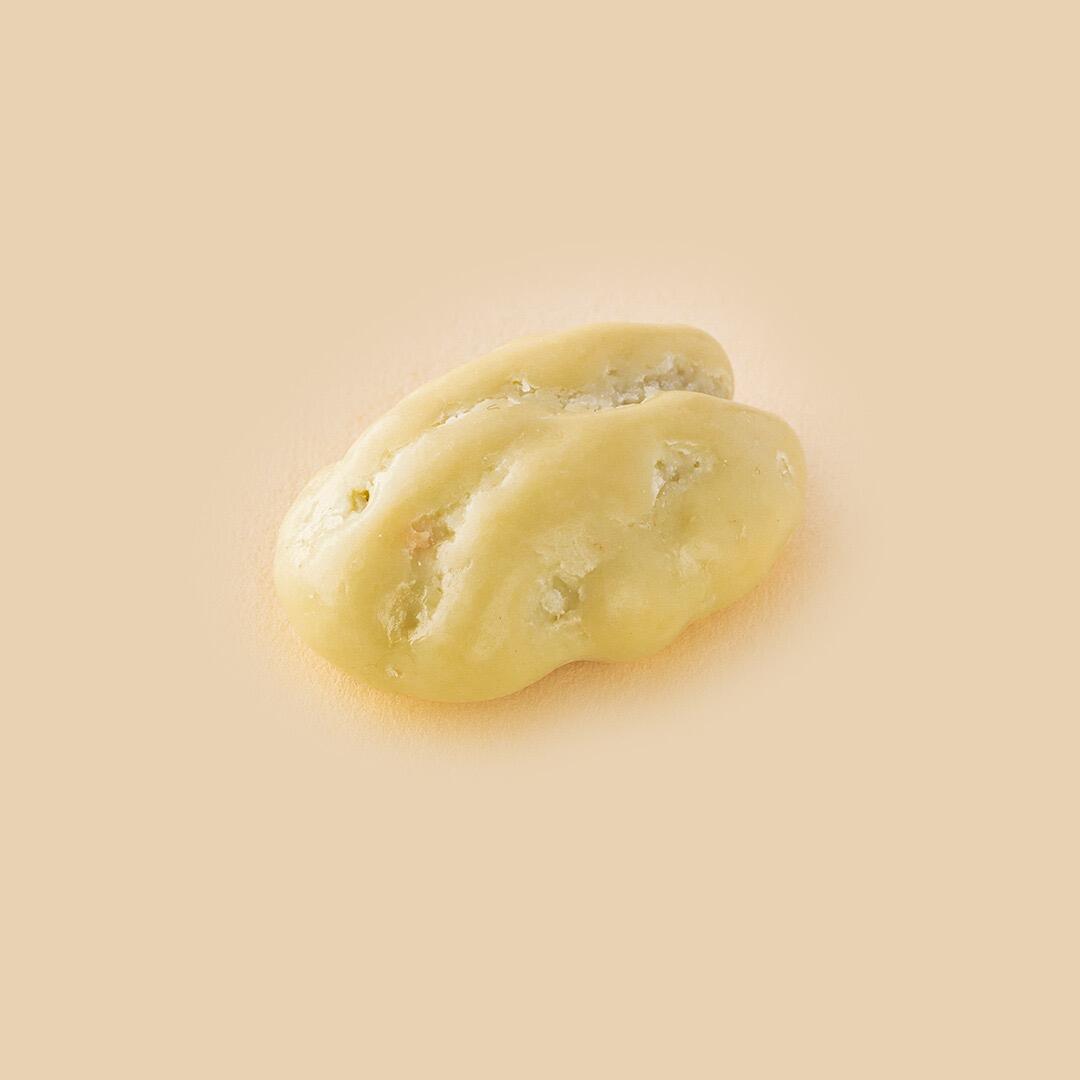 A single pecan nut coated in smooth, creamy white chocolate, centered against a plain light beige background, viewed from a slightly elevated angle.