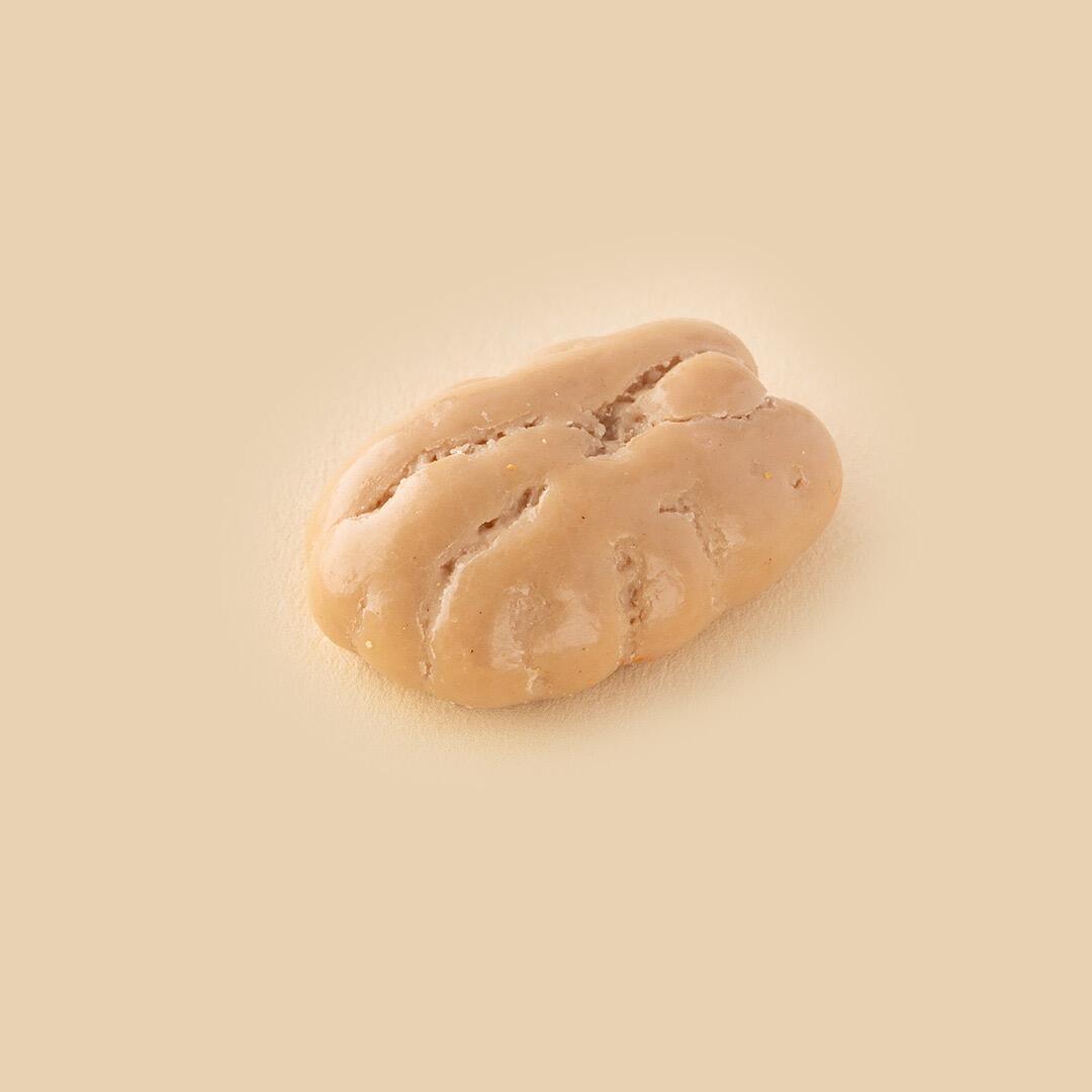 A single cappuccino-flavored chocolate-coated pecan nut centered on a solid beige background, viewed from a slightly elevated angle.