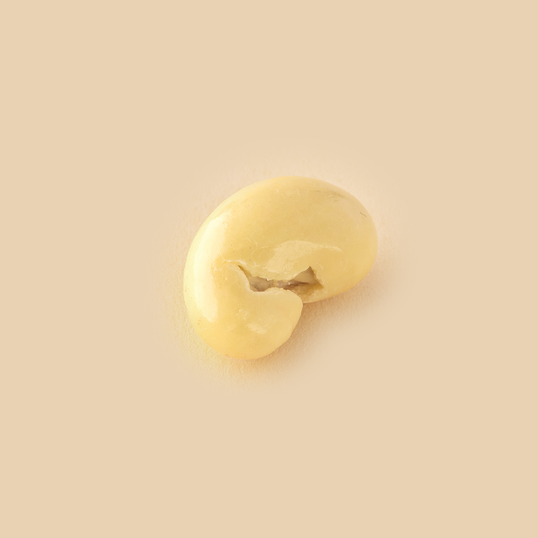 A single cashew nut coated in smooth white chocolate, isolated on a solid light beige background, shot from a top-down angle