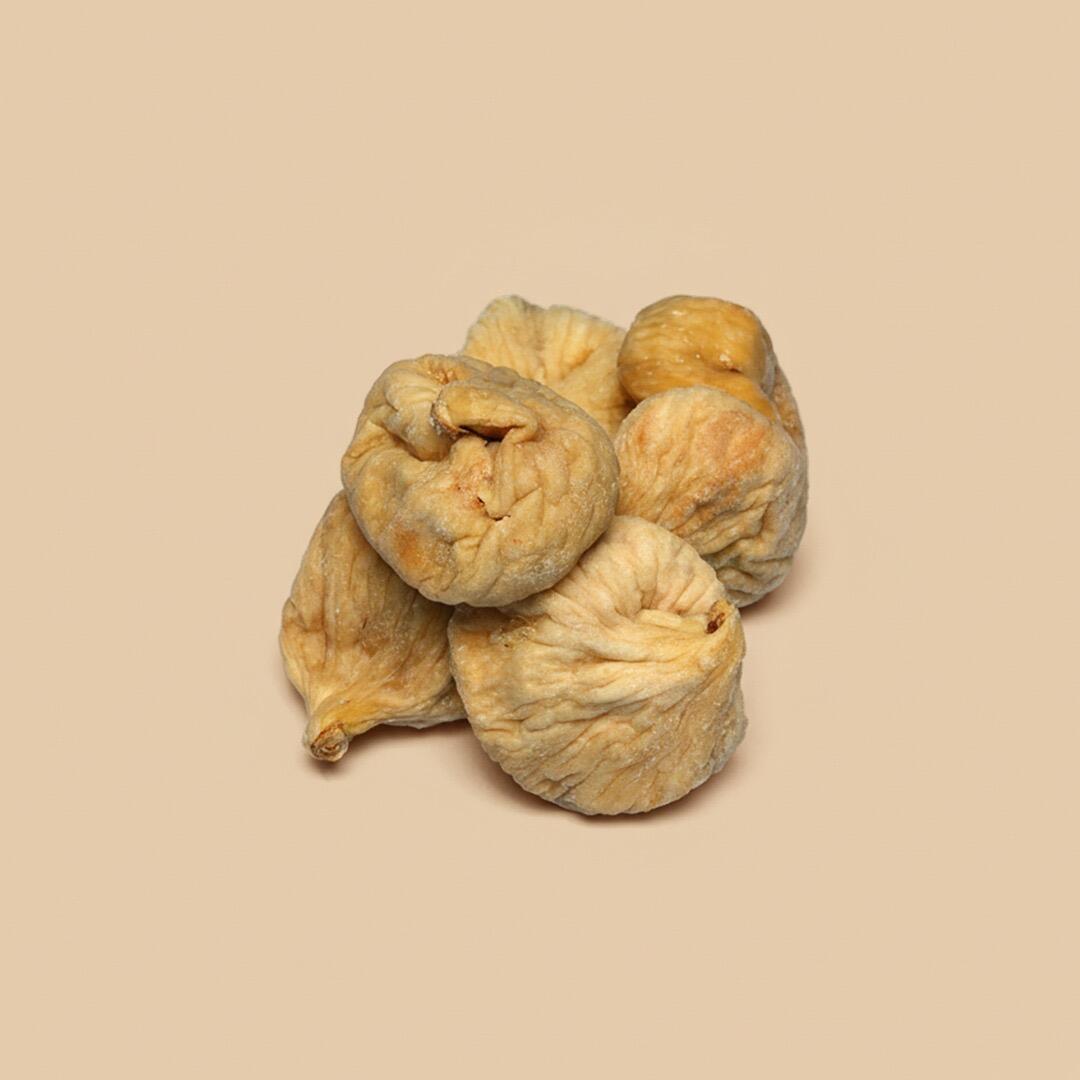 A small heap of several light-brown, wrinkled dried figs arranged in a pyramid shape on a solid soft-beige background viewed from a high angle
