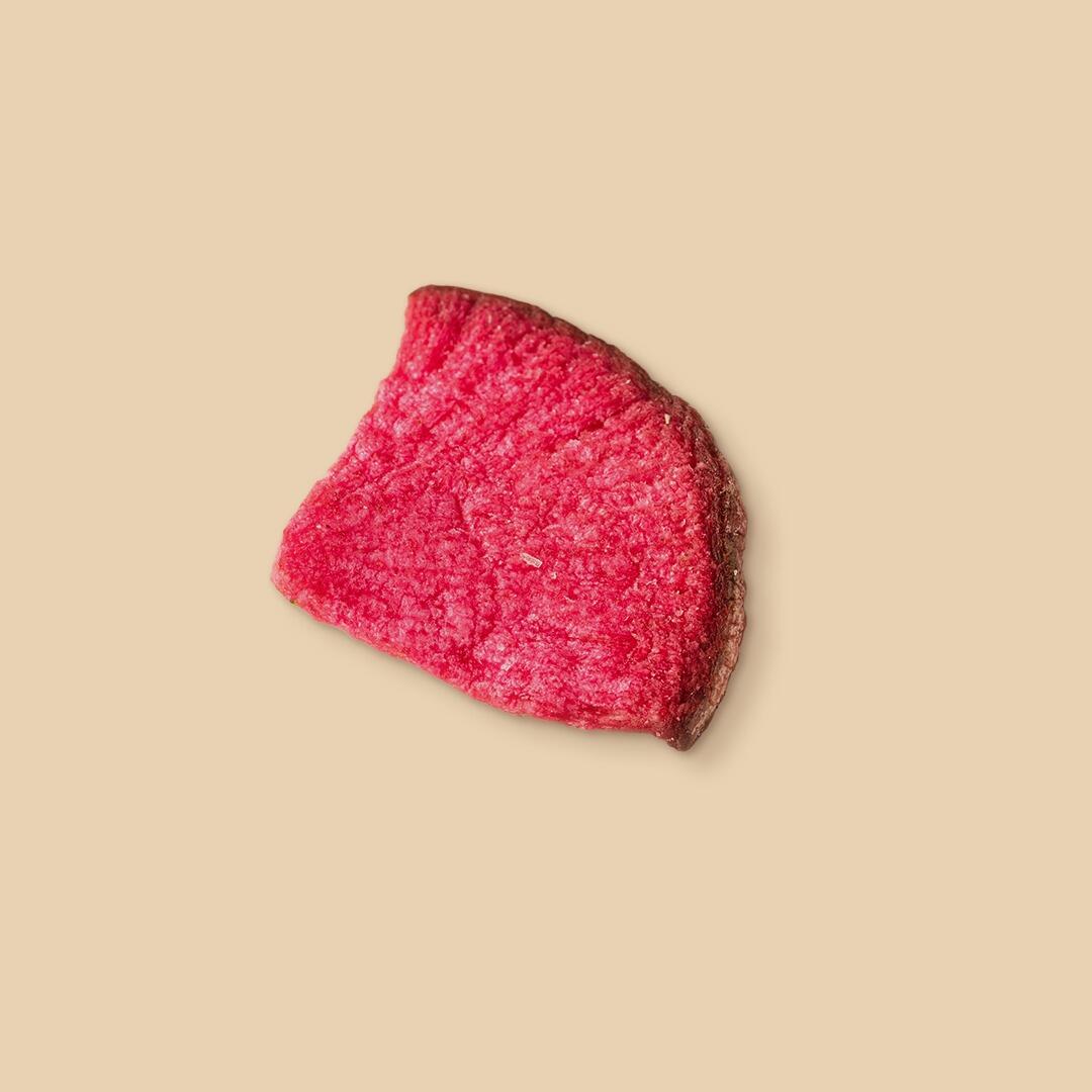 A single slice of vibrant deep-pink dehydrated radish with a textured surface, captured from a top-down angle against a plain light beige studio background.