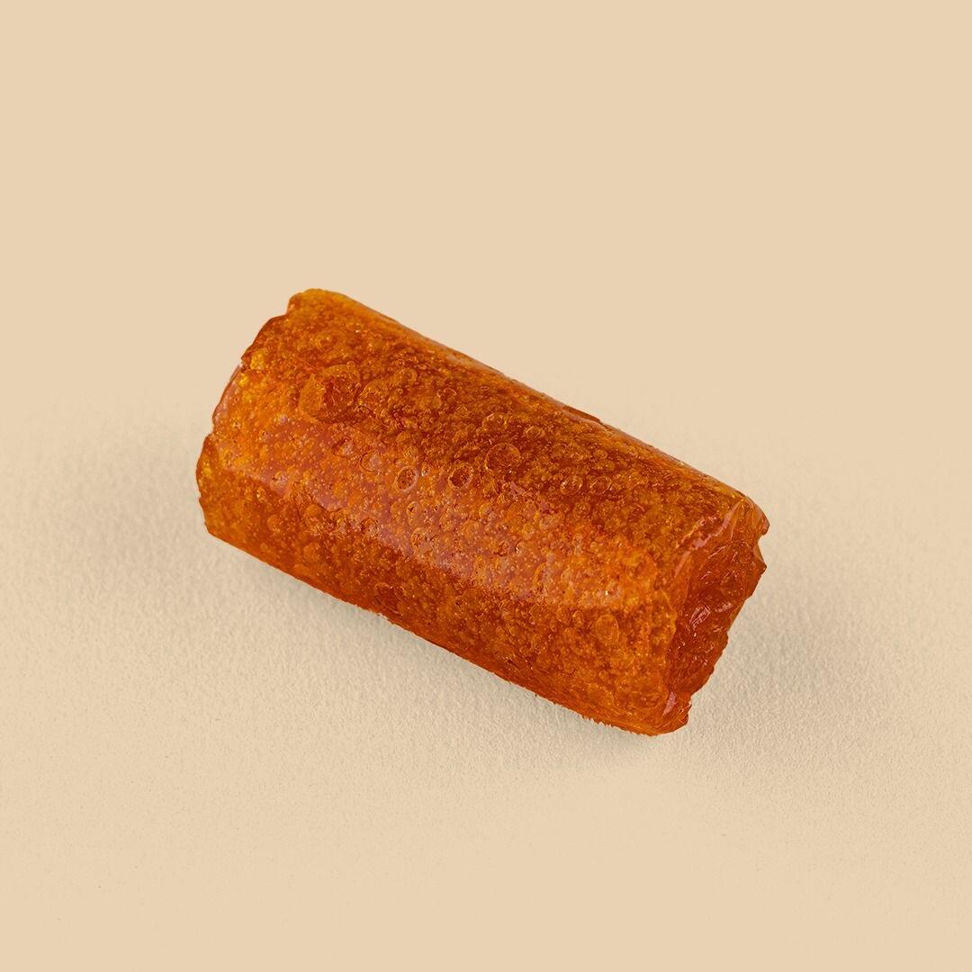 A cylindrical piece of translucent, amber-colored dried apricot paste, Qamar Al-Deen, captured from a high-angle view on a solid beige background