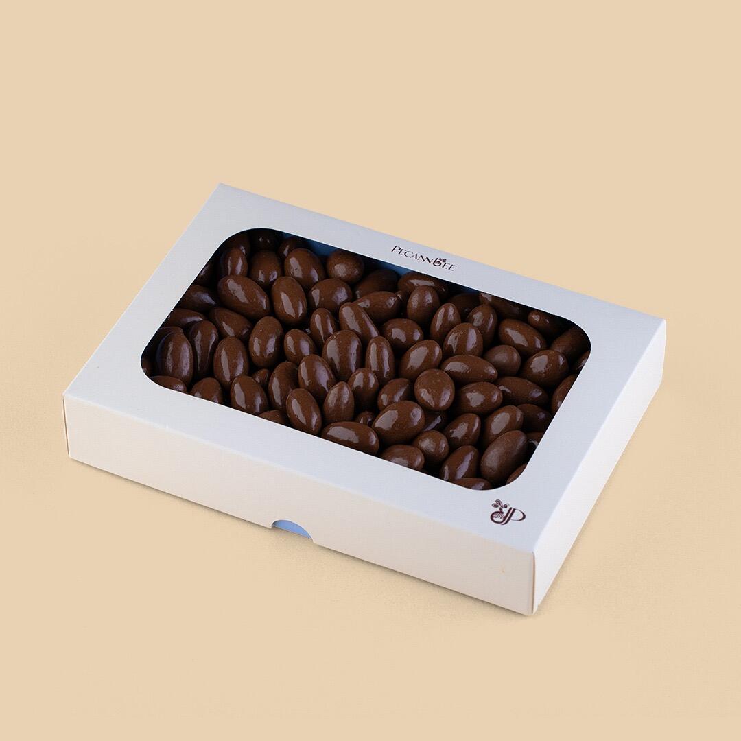 A rectangular white window box filled with brown chocolate-coated almonds, viewed from a high angle against a plain light beige background