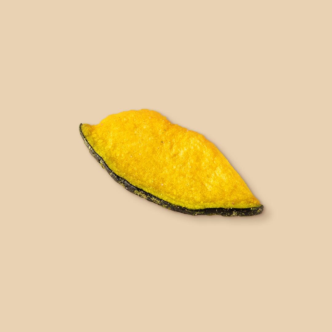 A single slice of dehydrated pumpkin featuring a bright yellow flesh and a thin, dark green outer rind, isolated against a solid beige background.