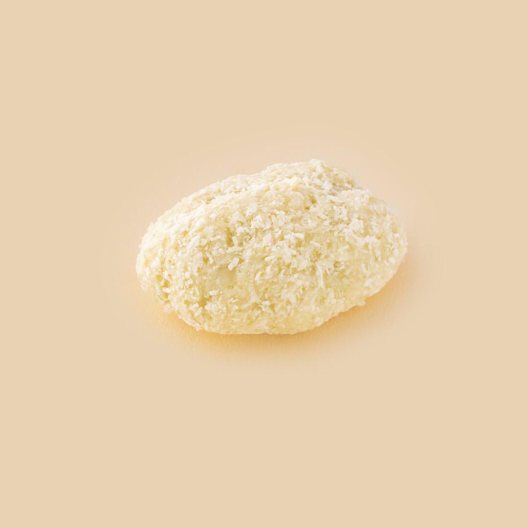 A single oval-shaped pecan dragée coated in creamy white chocolate and sprinkled with shredded coconut, centered against a solid light beige background
