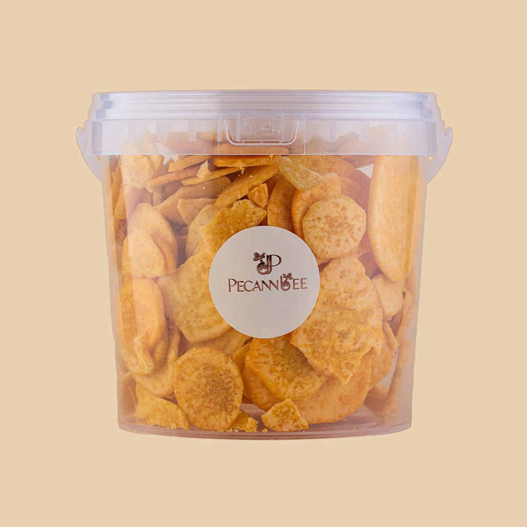 Clear plastic container filled with golden-orange dehydrated sweet potato chips, centered front view on a plain light beige background with PecanBee label