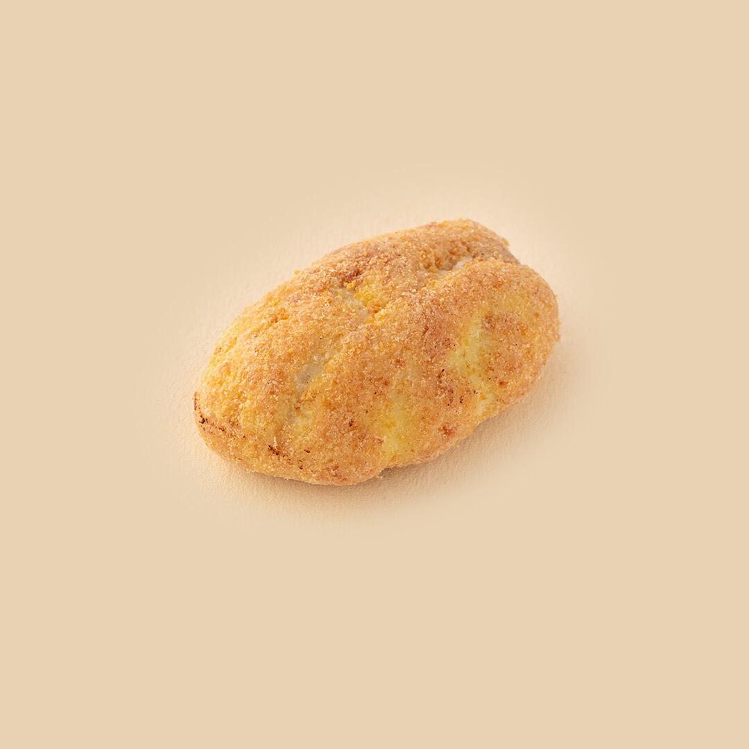 A single oval-shaped cookie coated in a golden-brown textured crumb, centered against a soft beige studio background.